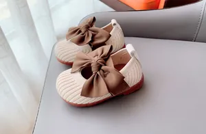 Close-up of beige knit Mary Janes with dark brown satin bow and non-slip rubber soles