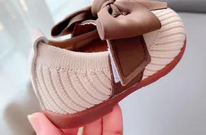 Macro detail of toddler knitted shoe featuring a large brown bow and non-slip rubber sole