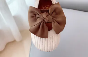Close-up of beige knit girl's shoes featuring a large brown silk bow decoration