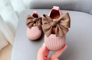 Close-up of pink knit baby walking shoe featuring a large brown satin bow detail
