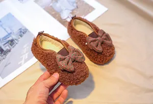 Detailed close-up of brown plush toddler shoes with a green polka dot bow and warm fleece lining
