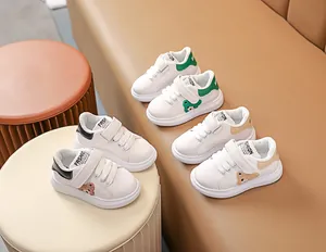 Trois paires de baskets blanches pour bébés avec écussons d'ours et scratchs sur un canapé