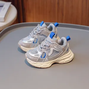Silver mesh kids running shoes with blue accents and thick soles on a grey display plate