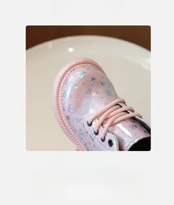 Détail de botte fille en cuir verni rose brillant avec cœur pailleté et lacets tressés