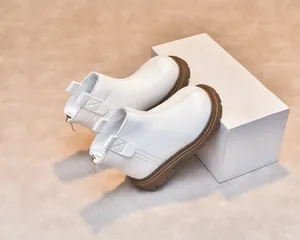 Close-up detail of white leather kids' boots with brown thick sole and back zipper
