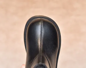 Close-up of black leather kids boots showing toe stitching and anti-slip sole texture