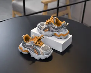 Macro view of grey mesh fabric and yellow leather stitch details on chunky kids sneakers