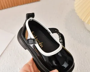Detalle de zapatos de charol negro para niña con tira de strass y ribete blanco