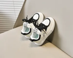 Détail de baskets blanches pour enfants en cuir avec lacets noirs et étiquette 2025