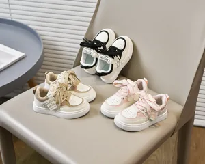 Détail de trois baskets pour enfants en noir, kaki et rose disposées sur une chaise en cuir