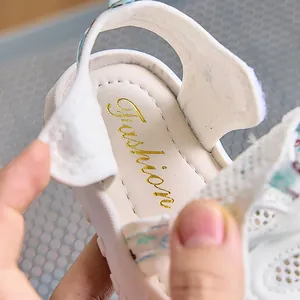 Dettaglio dei sandali bianchi per bambini con cinturino floreale e logo dorato interno