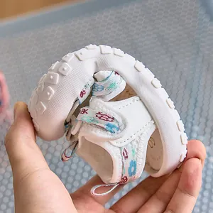 Sandali flessibili bianchi per neonati a fiori che mostrano la suola in gomma morbida
