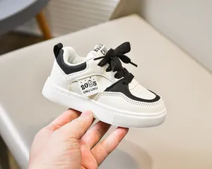 Détail de baskets en cuir blanc pour enfants avec lacets noirs et étiquette 2025