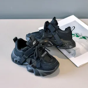 Detail view of children's black leather sneakers featuring velcro straps and chunky soles