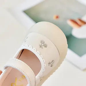 Nahaufnahme cremefarbener Mary Jane Babyschuhe mit filigraner Kirschstickerei und Texturen