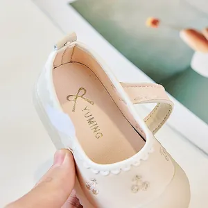 Details von cremefarbenen Baby-Mary-Janes mit Wellenrand und Kirsch-Stickerei