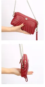 Detail of red leather crossbody bag with white stitching and floral metal ornament