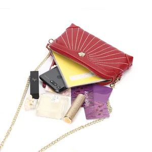 Red leather crossbody bag with white stitching and gold insect accent shown with essentials