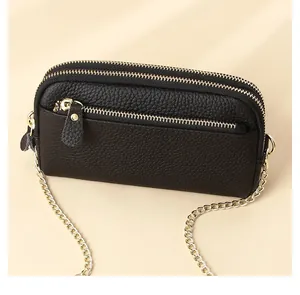 Detail of black pebbled leather crossbody phone bag with three gold zipper compartments