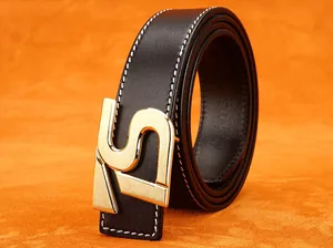 Dettaglio di cintura in pelle nera con fibbia dorata a forma di H e cuciture bianche