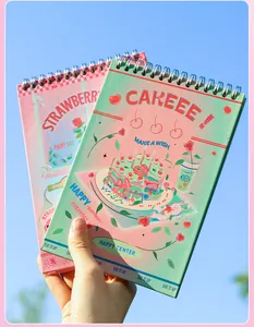 Nahaufnahme von Spiralnotizbüchern mit Erdbeer- und Tortenmotiven vor blauem Himmel