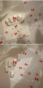 Detail of 3D Christmas nail stickers with red bows and gold snowflakes on white tips