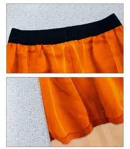 Detail of orange satin fabric showing black elastic waistband and wavy hemline edges