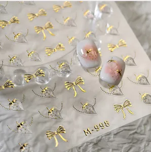 Detailed macro view of gold-stamped bow and strawberry nail stickers on carrier sheet M-998