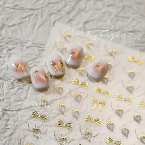 Macro detail of 3D gold bow and strawberry nail art stickers on white manicure tips