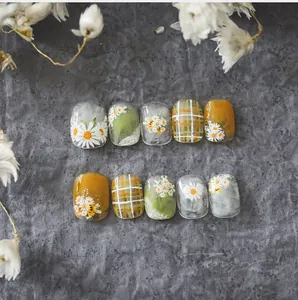 Detail of 10-piece handmade daisy press-on nails with plaid patterns and green hues
