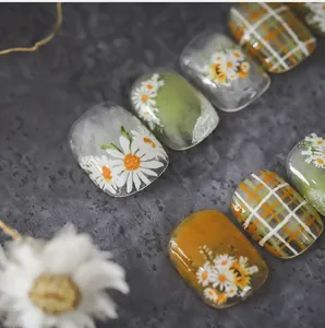Detail of short square press-on nails with daisy floral prints and green plaid patterns