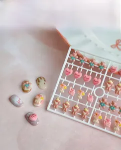 Detail of cute bear and heart resin nail charms on white stand with application example