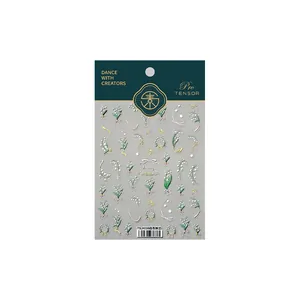 Stickers à ongles 3D muguet blanc avec nœuds dorés présentés sur emballage cartonné