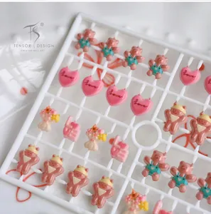 Macro detail of pink resin nail charms with 3D bears and love hearts on a white frame