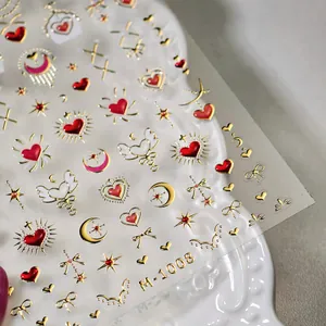 3D gold foiled nail decals featuring red hearts, stars and moons on white ceramic plate