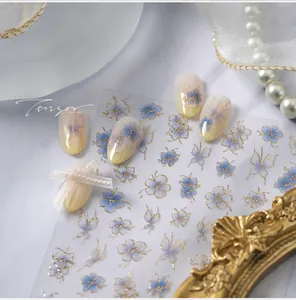 Détails d'autocollants pour ongles fleurs bleues et papillons dorés sur faux ongles