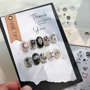 Detail shot of handmade nail tips with hand-painted panda and apple art on textured card