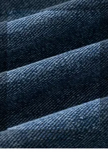 Détail en gros plan du tissu denim délavé dégradé montrant le tissage sergé et la texture
