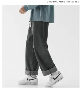 Detail of loose dark grey denim pants featuring white drawstring and cuffed leg hem