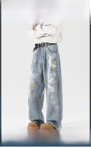 Detail of loose fit light blue jeans featuring colorful paint splatters and distressed texture