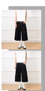 Model wearing dark denim wide-leg cropped jeans with a white vest in a modern room