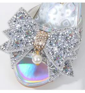 Detalle de sandalias plateadas de niña con lazo de strass y acabado irisado brillante