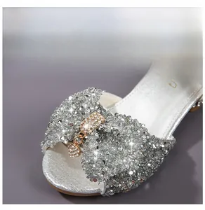 Detail of silver sequined girls sandals with a large rhinestone bow and heart pendant