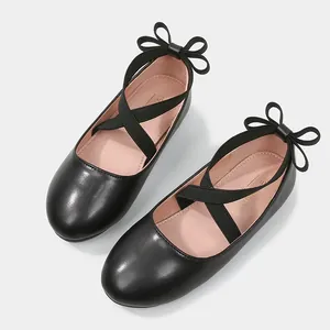 Girl's black leather flat shoes with elastic cross straps and bow detail on the heel