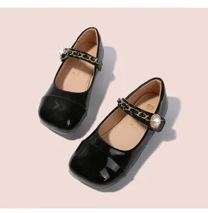 Detailansicht der schwarzen Lackleder-Mary-Janes mit Perlenschnalle und goldener Kette