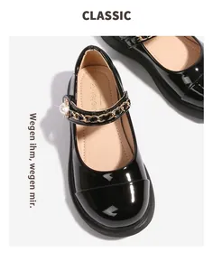 Détail de Mary Janes en cuir verni noir avec chaîne dorée et perle sur la bride