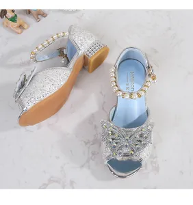 Close-up of girls silver sequined sandals with rhinestone bow and pearl ankle strap