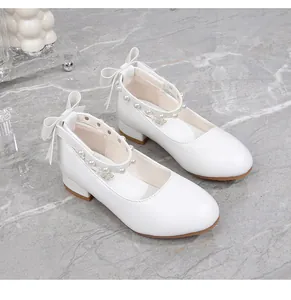 Detail of white girls princess shoes with pearl straps and bow decorations on the heel