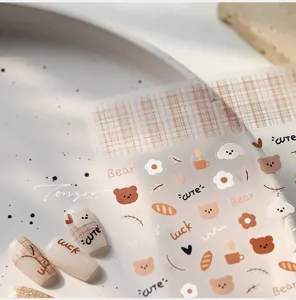 Detail of cute bear and coffee nail art stickers applied on creamy white manicured nails