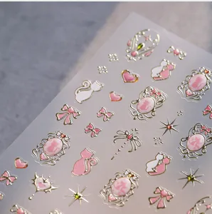 Macro shot of 3D embossed nail stickers featuring pink bows, cats, and gold gilded edges